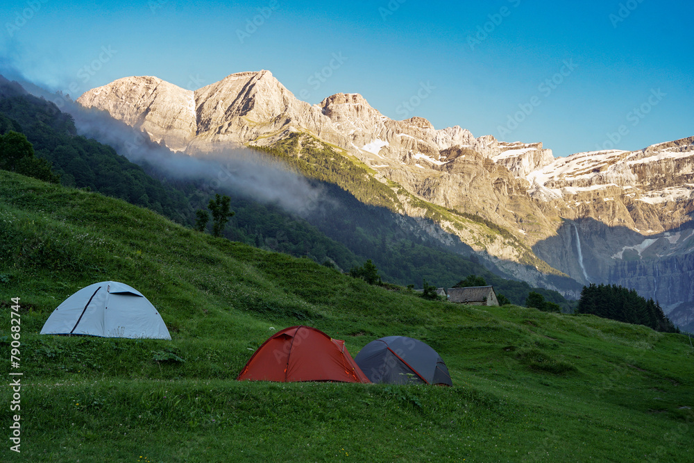 Three tents on meadow in high mountains during sunset in french Pyrenees near Gavarnie Falls waterfall, France, popular hiking destination
