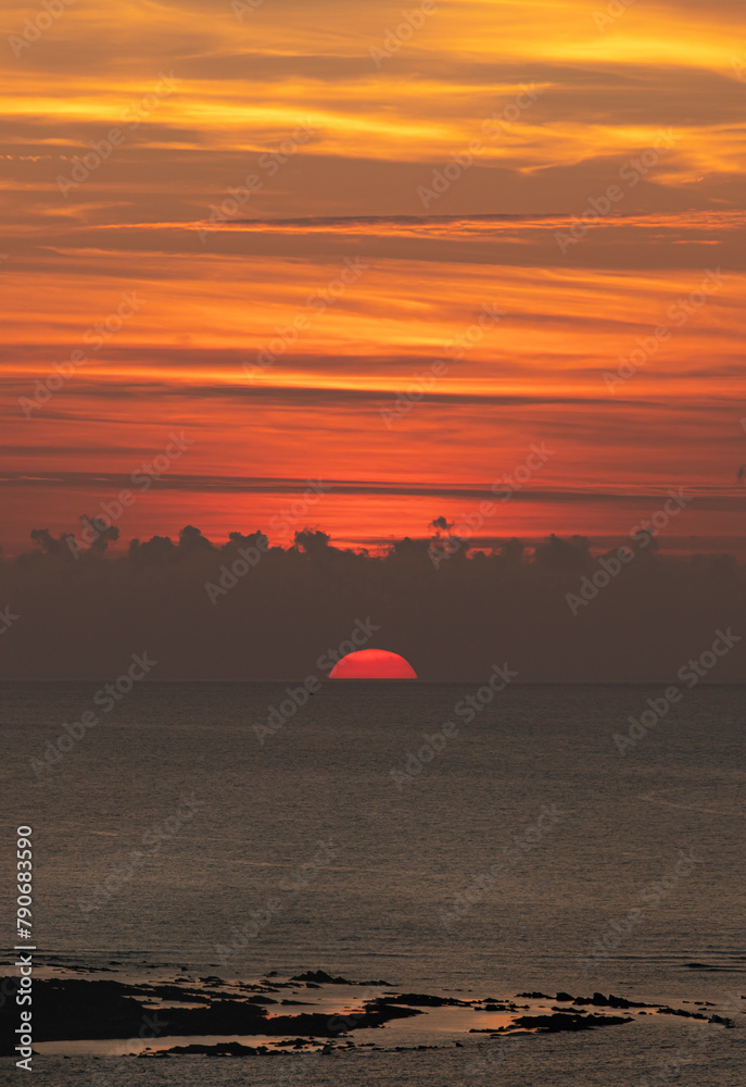 SUNSET AT SEA WITH A BEAUTIFUL RED SUN IN THE HORIZON READY TO HIDE SURROUNDED OF NICE CLOUDS