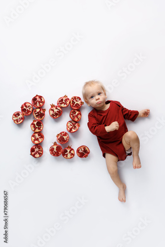 twelve month old infant on white background with red pomegranate