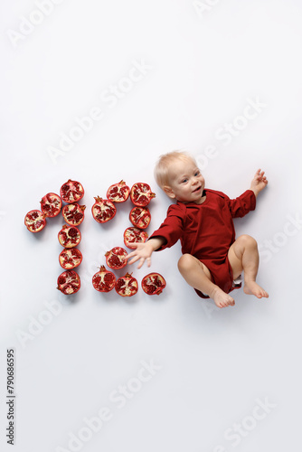 twelve month old infant on white background with red pomegranate
