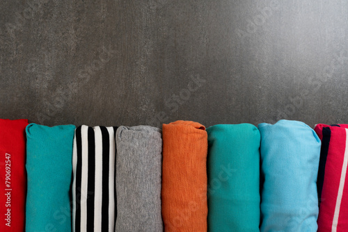 close up of rolled colorful t shirt clothes on black table background, travel and lifestyle concept