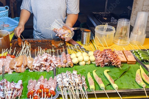 Fototapeta Naklejka Na Ścianę i Meble -  Bustling street food stall showcases skewered delicacies, from tantalizing seafood to traditional meats, ready to entice passersby with aromatic, grilled treats. Street food and small business concept