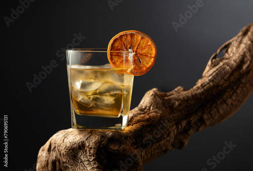 Old fashioned cocktail with ice and dried orange slice on a old snag. © Igor Normann