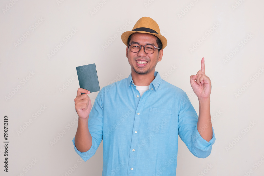 A man wearing beach hat smiling and pointing up while holding passport document A man wearing beach hat smiling and pointing up while holding passport document