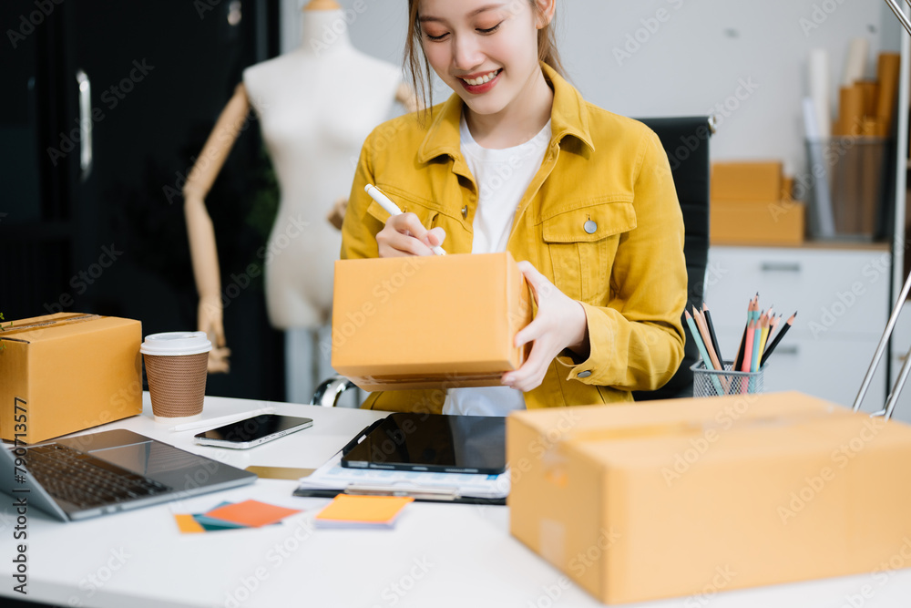 Young business owner woman prepare parcel box and standing check online orders for deliver to customer on tablet, laptop Young business owner woman prepare parcel box and standing check online orders for deliver to customer on tablet, laptop