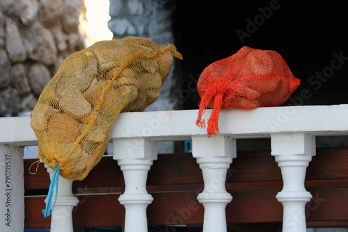 Two yellow and red reusable nylon mesh produce bags filled with old bread leftovers on concrete balcony fence left to dry on warm sunny autumn day