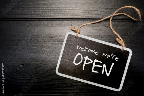 Small black chalkboard sign on black wood background with text handwritten Welcome We're Open, concept of open new business, opening sign to inform customers, start new business