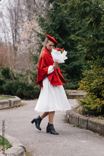 Vertical photo young woman in red french beret and jacket dressed white dress, walking in city park with bouquet bunch of fresh spring tulips flowers, celebrating International Women's Day, holiday 