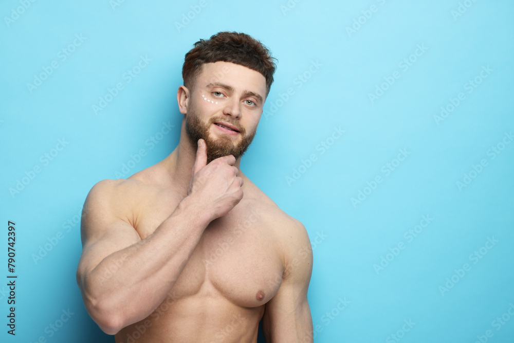 Fototapeta premium Handsome man with moisturizing cream on his face against light blue background, space for text