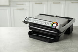 Electric grill on grey textured table in kitchen, closeup with space for text. Cooking appliance