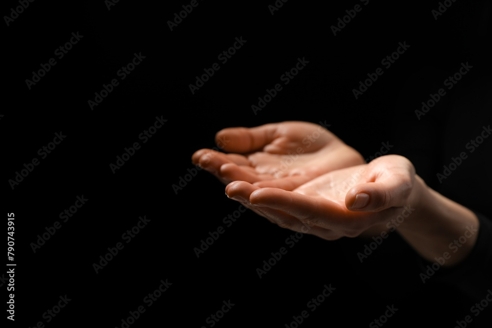 Fototapeta premium Religion. Woman with open palms praying on black background, closeup. Space for text