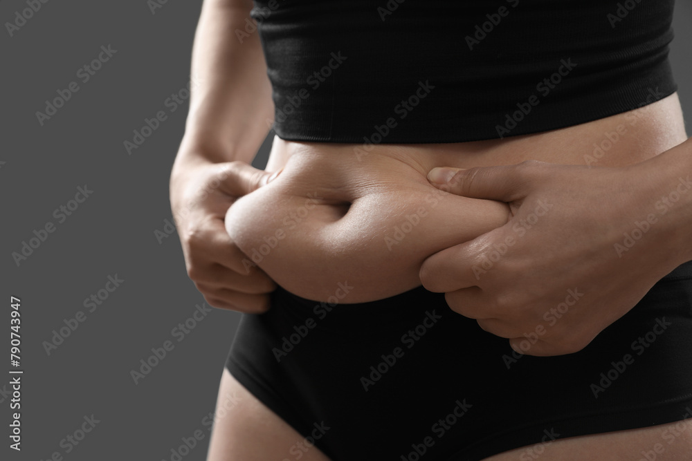 Fototapeta premium Woman touching belly fat on grey background, closeup. Overweight problem