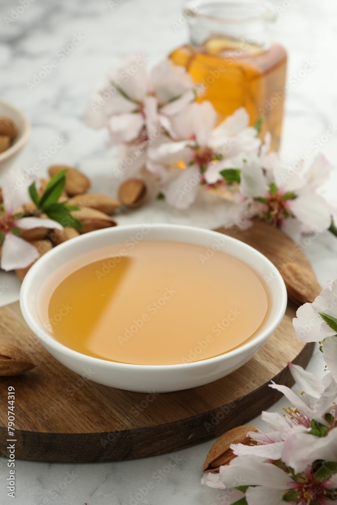 Almond oil in bowl, nuts and flowers on white marble table, closeup Almond oil in bowl, nuts and flowers on white marble table, closeup