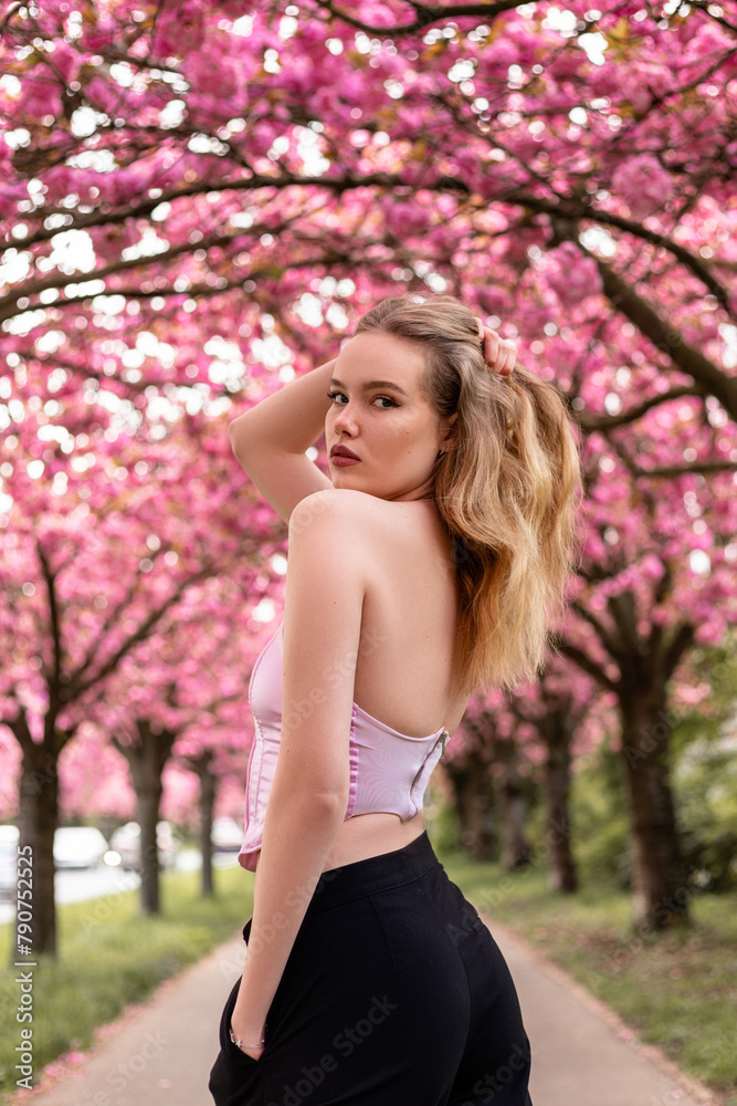 Woman standing on sakura alley with her back turned and adjusting her hair Woman standing on sakura alley with her back turned and adjusting her hair