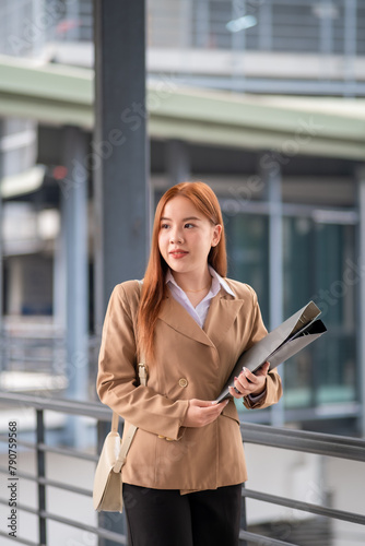 Happy young Asian female businesswoman using cell phone smartphone and holding document files phone at the walkway