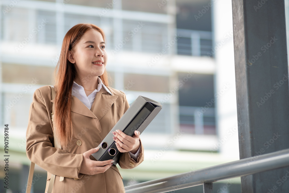 Happy young Asian female businesswoman using cell phone smartphone and holding document files phone at the walkway
