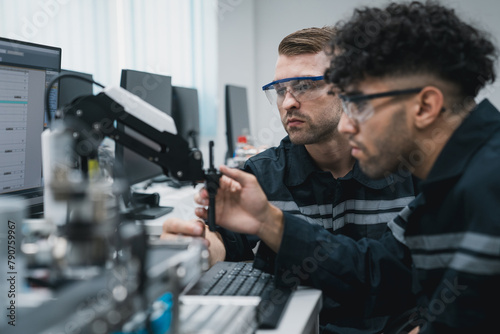 Engineering student assembling a robotic arm using a computer in a technology workshop. Service engineer holding a robot controller and inspecting the robotic arm s welding hardware.