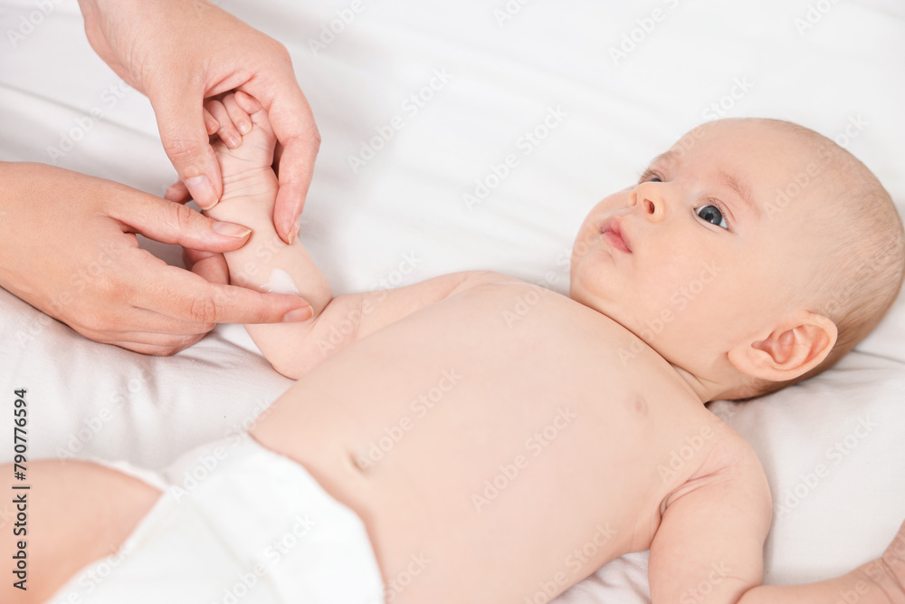Woman applying body cream onto baby`s skin on bed, closeup Woman applying body cream onto baby`s skin on bed, closeup