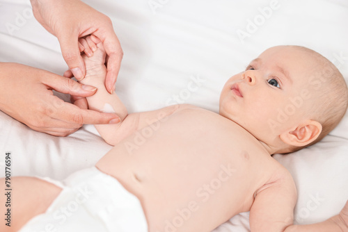 Woman applying body cream onto baby`s skin on bed, closeup