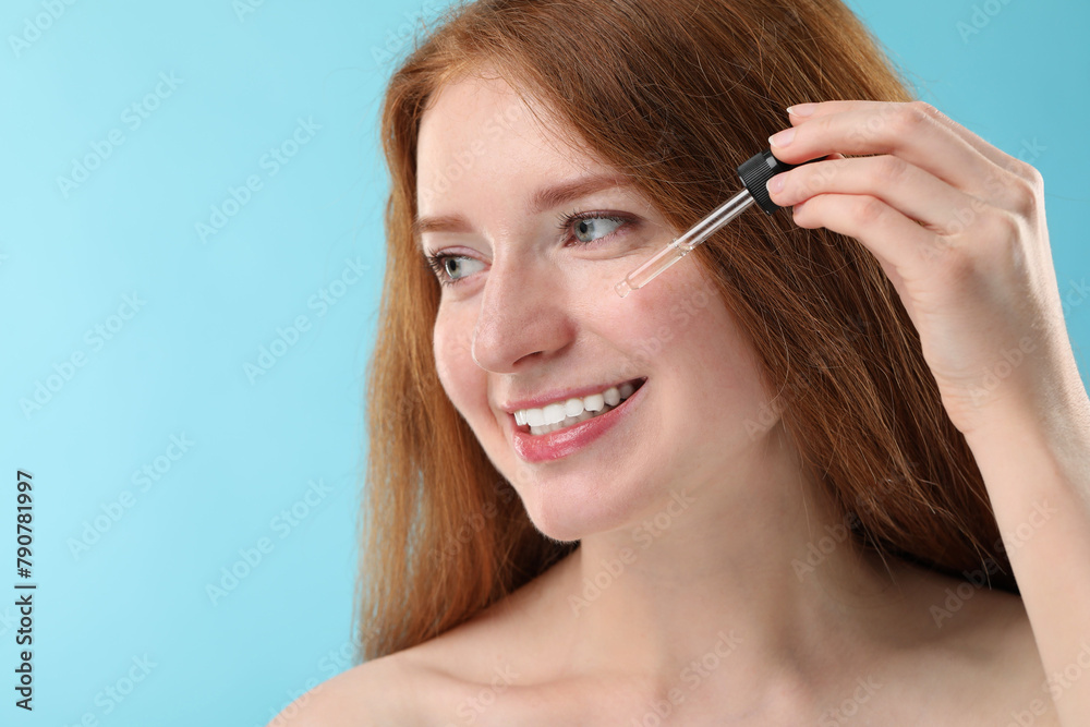 Smiling woman with freckles applying cosmetic serum onto her face against light blue background, closeup. Space for text Smiling woman with freckles applying cosmetic serum onto her face against light blue background, closeup. Space for text