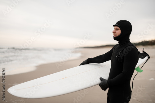 Smiling male surfer standing on the sandy seashore with a white surfboard in his hands