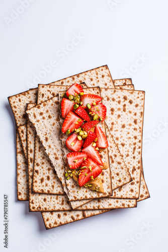 Matza toast with peanut butter, strawberries and pistachios on a white plate. Traditional bread for the Jewish holiday of Passover.