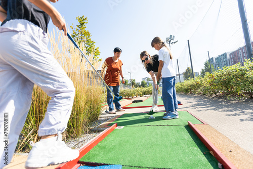 Cute school girl playing mini golf with family. Happy toddler child having fun with outdoor activity. Summer sport for children and adults, outdoors. Family vacations or resort. photo