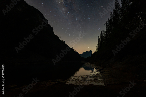 It is a stunning sight as the Milky Way towers over a large pond in a quarry.On one side is a pine forest and on the other is a mountain. The reflection of the stars in the water at night