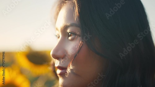 Closeup face of Asian woman opening eyes on sunset background. Young female looking straight at the sunflower field landscape