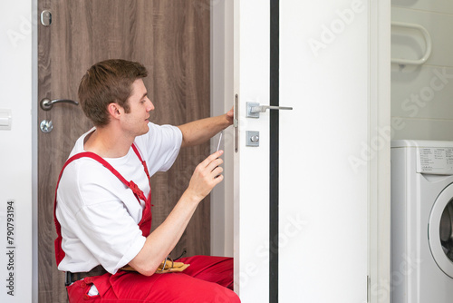 Young handyman installing a white door with an electric hand drill in a room
