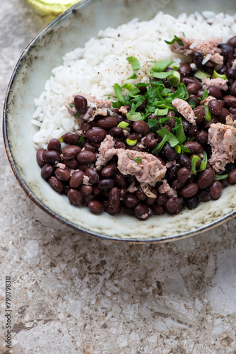 Black beans with chicken meat and white rice, vertical shot on a light-brown granite background, middle closeup