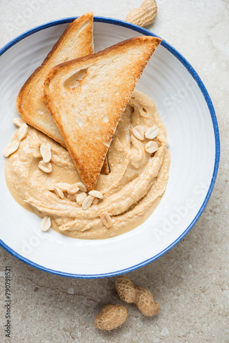 Blue and white plate with peanut butter and toasts, vertical shot on a beige stone background, elevated view, middle close-up