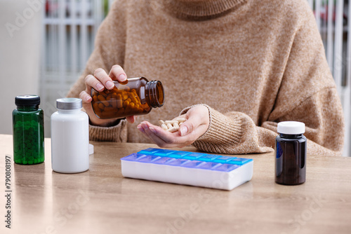 Female putting prescription pills and vitamins in a daily pill box organizer. Sorting nutritional supplements and antibiotics into weekly pills container.