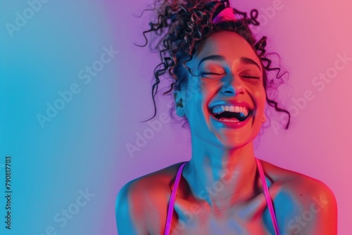 Joyful woman with curly hair laughing against vibrant pink and blue background photo
