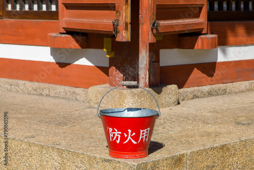 a red bucket with the japanese inscription "for fire protection" in front of an old wooden building