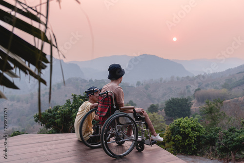 A confident young man on wheelchair and parent, caregiver or volunteer with lighting sunset, Happy family time and learning on the natural park,Travel on vacation with family, Mental health concept.