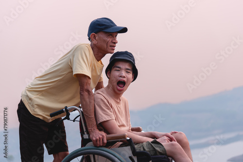 A confident young man on wheelchair and parent, caregiver or volunteer with lighting sunset, Happy family time and learning on the natural park,Travel on vacation with family, Mental health concept.