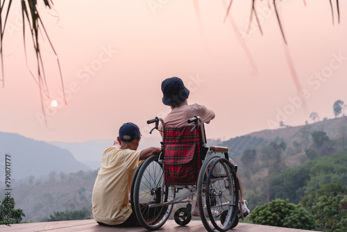 A confident young man on wheelchair and parent, caregiver or volunteer with lighting sunset, Happy family time and learning on the natural park,Travel on vacation with family, Mental health concept.