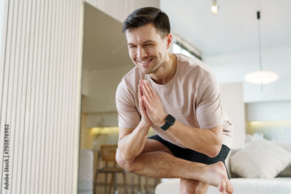 Fototapeta premium Man in a balanced yoga pose with hands in prayer position, exuding concentration and serenity in his home.