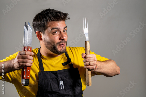Hombre cocinero feliz y entusiasmado sosteniendo sus utensillos de cocina. Fotografia de estudio con fondo blanco