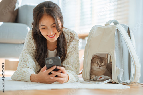 Happy asian woman using her mobile phone while a cat sleeping peacefully in her cat bag, Happy domestic animals at home.