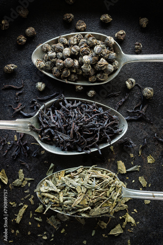 Various types of dried tea on spoons on a black background, top view