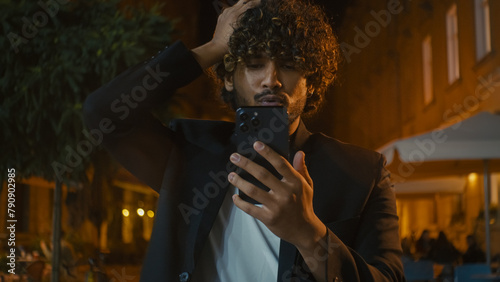 Indian Arabian Latino American man using mobile phone smartphone losing failure bad news messages annoyed dissatisfied unhappy guy hold head city outside evening mistake problem trouble breaking gen z