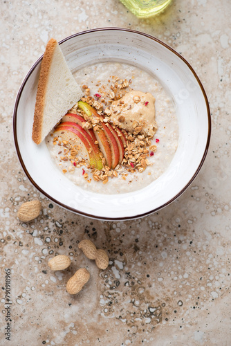 Bowl of oatmeal with peanut butter and fresh apple slices, above view on a beige granite background, vertical shot with space