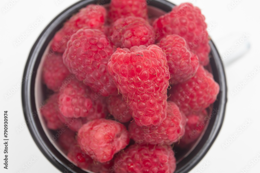 Freshly picked bright raspberries in a enamel mug Freshly picked bright raspberries in a enamel mug