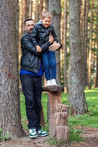 A father helps his son to get down from obstacle course on a forest fitness trail