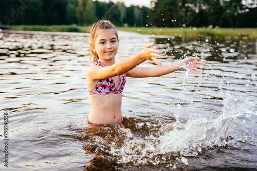 Girl splashing, play with water into lake at summer. Summertime children healthy vacation concept
