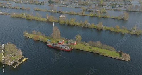 Aerial: Drone Panning Shot Of Ship Outside Houses On Green Landscape In Vinkeveense Plassen Lake - North Holland, Netherlands photo