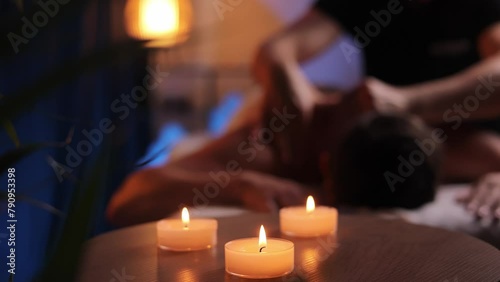 Male hands doing therapeutic neck massage for man lying on massage couch in relax massage spa salon in evening atmosphere. Point massage in the spa center. Body therapy for a healthy lifestyle.