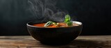A bowl of hot soup steaming on a wooden table against a black background.